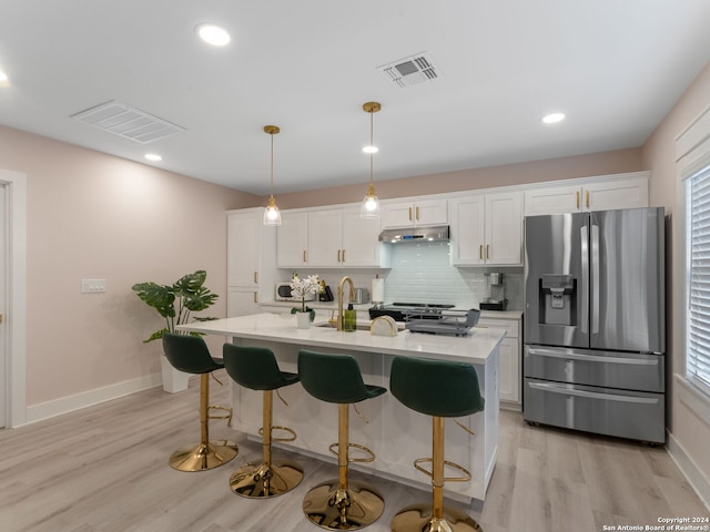 kitchen featuring stainless steel refrigerator with ice dispenser, an island with sink, pendant lighting, light hardwood / wood-style floors, and white cabinets