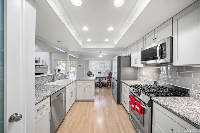 kitchen with white cabinets, sink, light wood-type flooring, ornamental molding, and stainless steel appliances