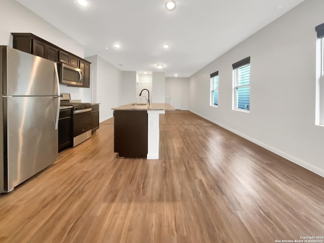 kitchen featuring appliances with stainless steel finishes, dark brown cabinetry, sink, light hardwood / wood-style floors, and an island with sink