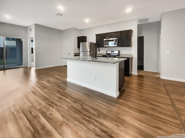 kitchen featuring light stone counters, an island with sink, dark wood-type flooring, and appliances with stainless steel finishes