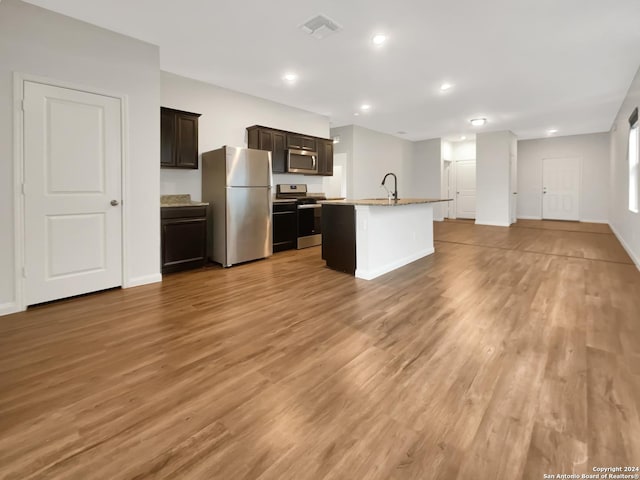 kitchen with sink, stainless steel appliances, a center island with sink, dark brown cabinets, and light wood-type flooring