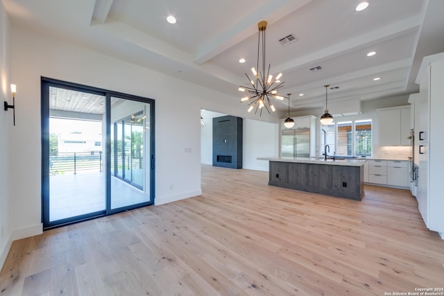 kitchen featuring light wood-type flooring, decorative light fixtures, white cabinets, built in fridge, and an island with sink