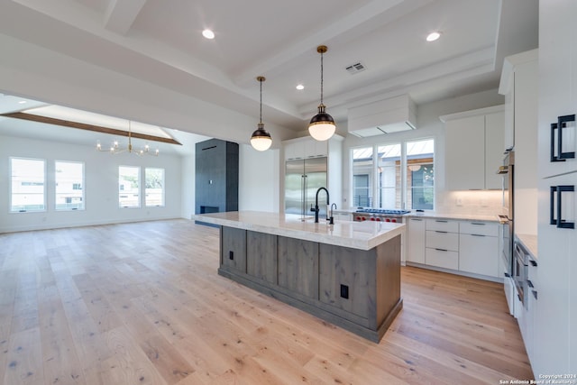 kitchen with stainless steel appliances, light hardwood / wood-style floors, decorative light fixtures, a kitchen island with sink, and white cabinets