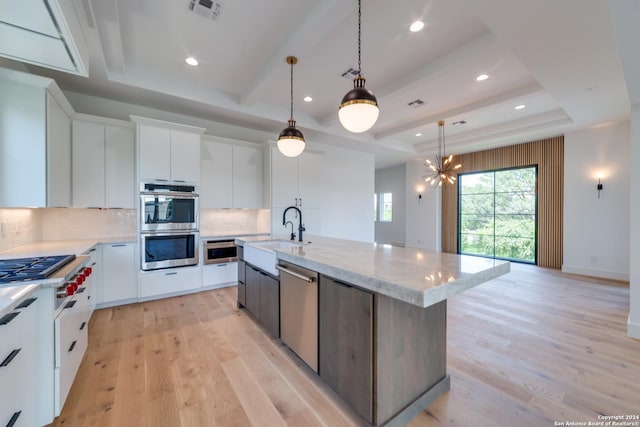 kitchen featuring white cabinets, sink, an island with sink, a tray ceiling, and light hardwood / wood-style floors