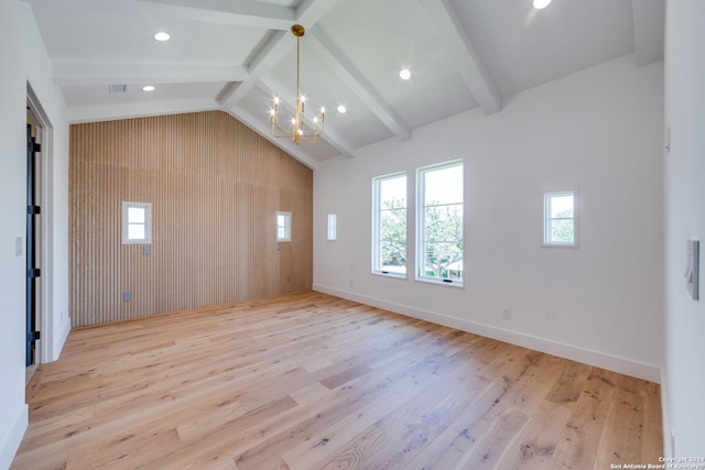 empty room featuring a chandelier, light hardwood / wood-style flooring, lofted ceiling with beams, and wood walls