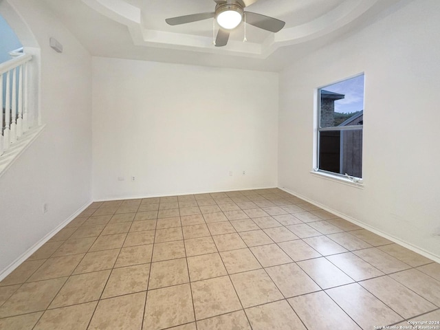 unfurnished room with ceiling fan, light tile patterned flooring, and a raised ceiling