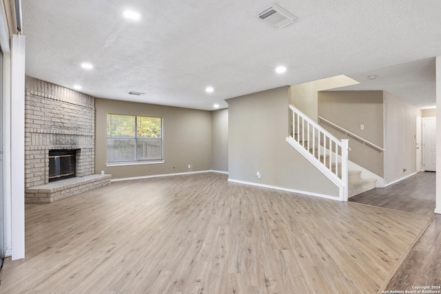 unfurnished living room with a brick fireplace, a textured ceiling, and light hardwood / wood-style flooring