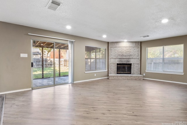 unfurnished living room featuring plenty of natural light, light hardwood / wood-style floors, and a brick fireplace