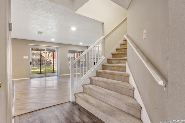 stairs featuring wood-type flooring and a textured ceiling