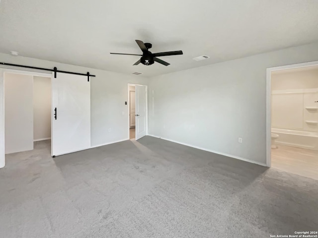 carpeted spare room with a barn door and ceiling fan