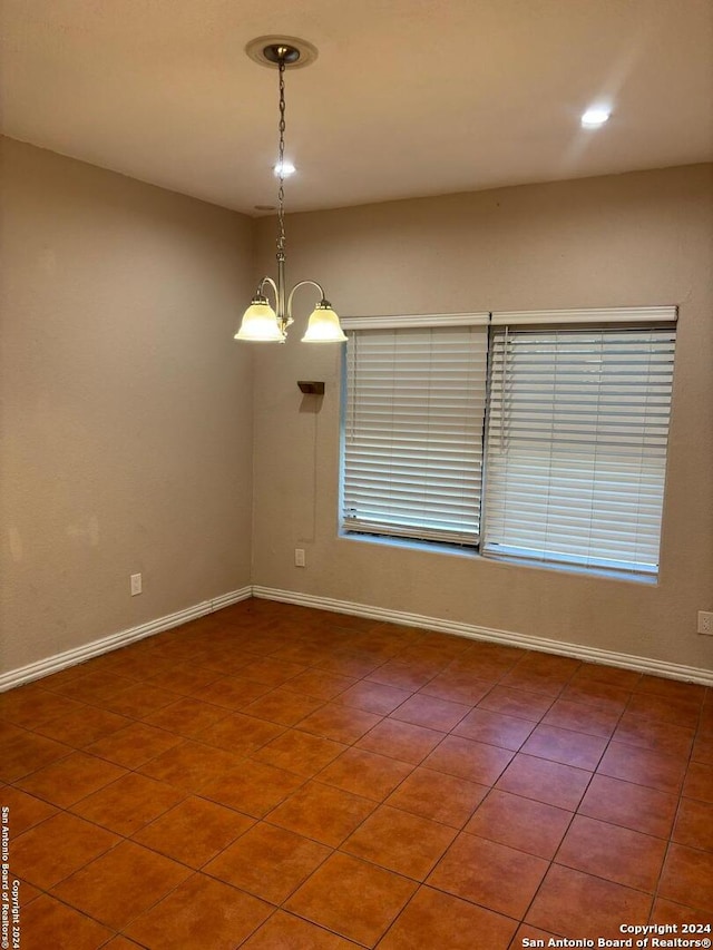 tiled empty room featuring an inviting chandelier