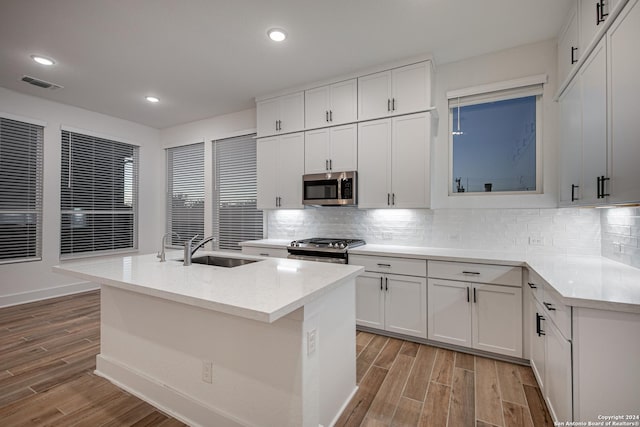 kitchen with a center island with sink, sink, light hardwood / wood-style floors, white cabinetry, and stainless steel appliances