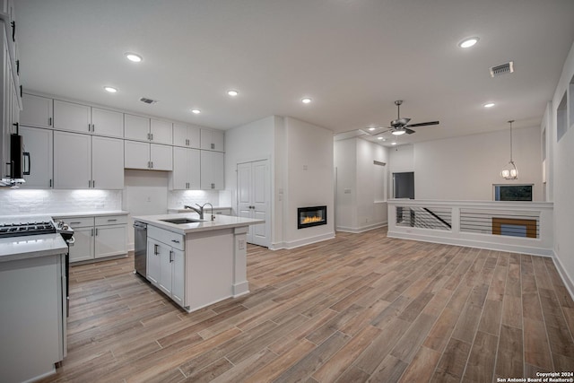 kitchen with sink, ceiling fan, light wood-type flooring, an island with sink, and white cabinetry