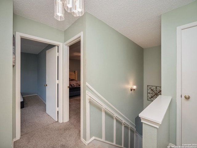 corridor with light carpet, a textured ceiling, and an inviting chandelier