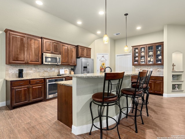 kitchen featuring lofted ceiling, a kitchen island with sink, light hardwood / wood-style floors, light stone counters, and stainless steel appliances