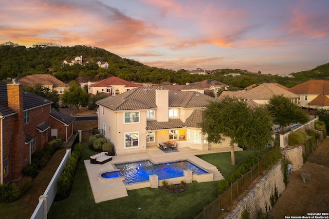 pool at dusk with an in ground hot tub, a yard, and a patio