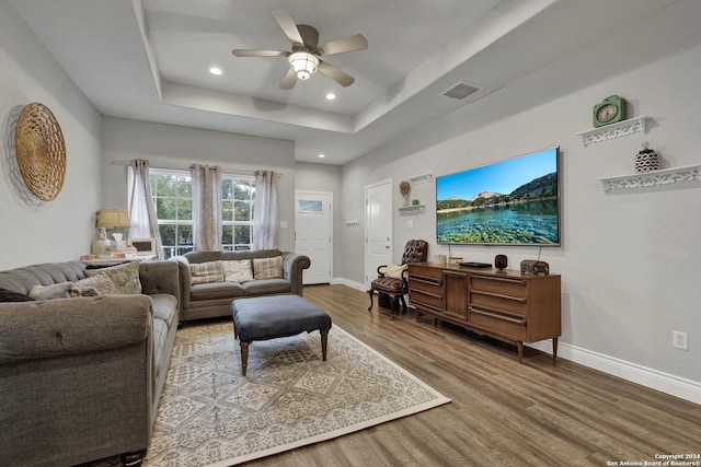 living room featuring hardwood / wood-style floors, ceiling fan, and a tray ceiling