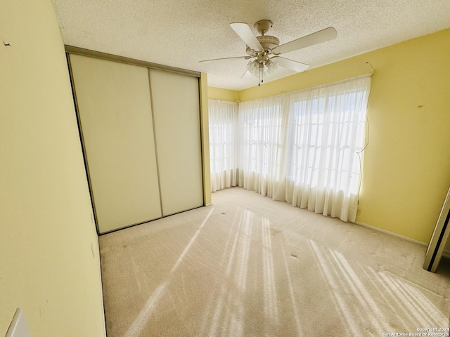 unfurnished bedroom with ceiling fan, a closet, light colored carpet, and a textured ceiling