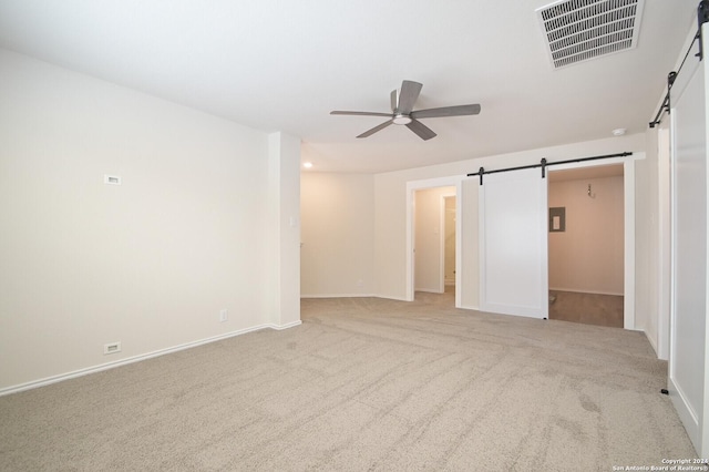 unfurnished room featuring ceiling fan, a barn door, and light colored carpet