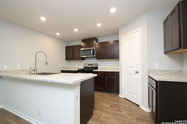 kitchen with kitchen peninsula, dark brown cabinetry, stainless steel appliances, sink, and hardwood / wood-style floors