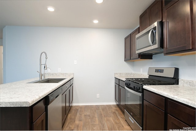 kitchen featuring dark brown cabinetry, sink, light hardwood / wood-style flooring, kitchen peninsula, and appliances with stainless steel finishes