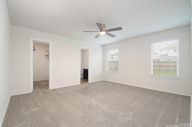 unfurnished bedroom featuring light carpet, a walk in closet, ensuite bath, ceiling fan, and a closet