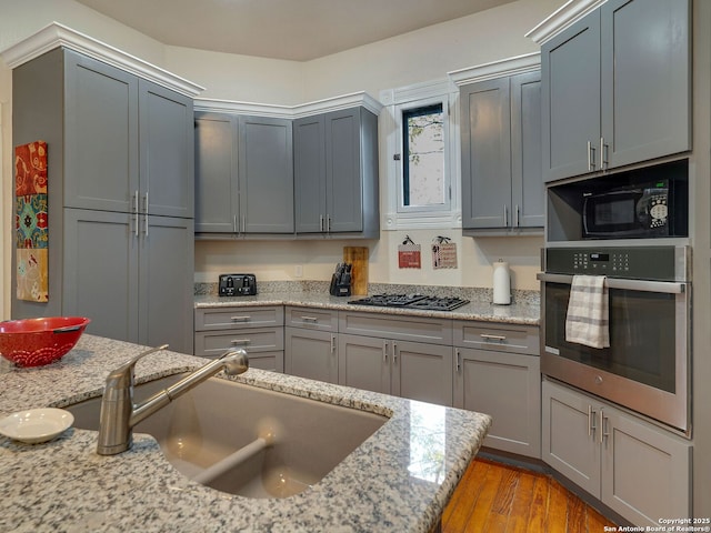 kitchen featuring light stone countertops, appliances with stainless steel finishes, gray cabinetry, sink, and light hardwood / wood-style floors