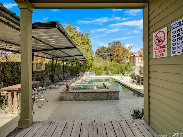 wooden terrace featuring a swimming pool with hot tub and a patio area