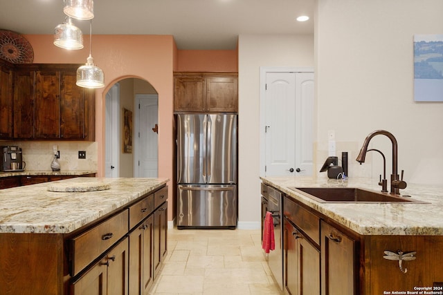 kitchen with backsplash, light stone counters, stainless steel appliances, sink, and a kitchen island