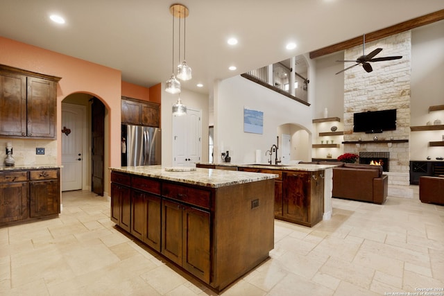 kitchen featuring a stone fireplace, hanging light fixtures, light stone countertops, a kitchen island, and stainless steel refrigerator