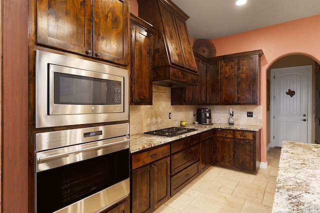 kitchen featuring tasteful backsplash, light stone counters, dark brown cabinets, and appliances with stainless steel finishes