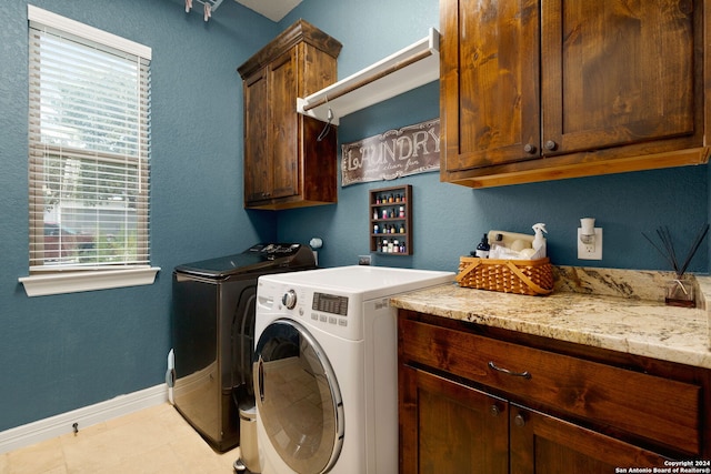 clothes washing area with separate washer and dryer, plenty of natural light, light tile patterned floors, and cabinets