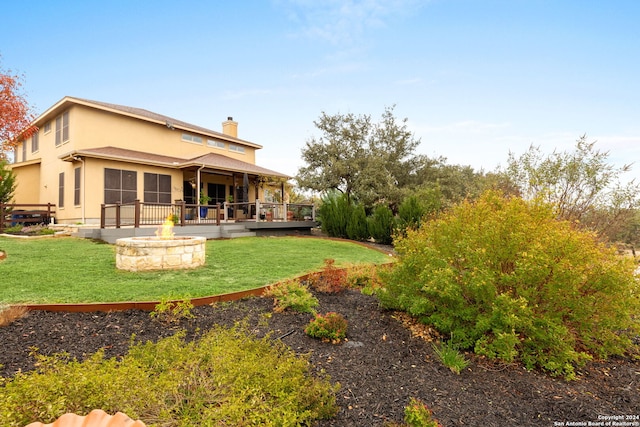 back of property featuring a wooden deck, a yard, and a fire pit