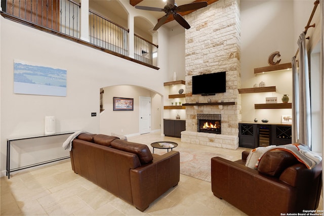 living room featuring a stone fireplace, ceiling fan, and a towering ceiling