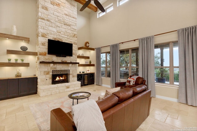 living room featuring a stone fireplace, ceiling fan, and a high ceiling