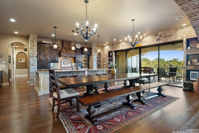 dining area with a stone fireplace, dark wood-type flooring, and a notable chandelier