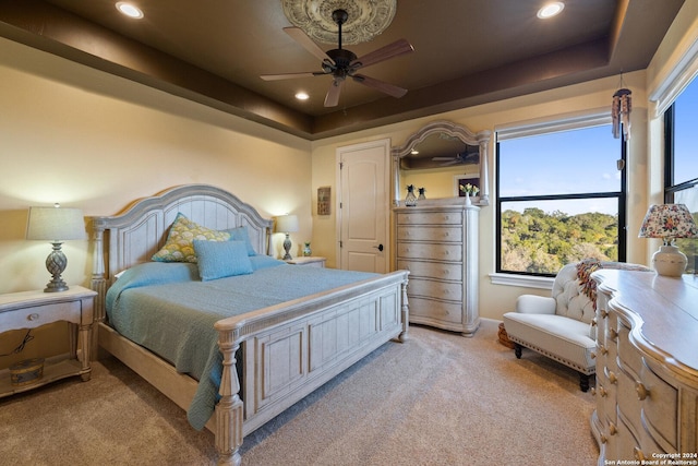 carpeted bedroom with ceiling fan and a tray ceiling