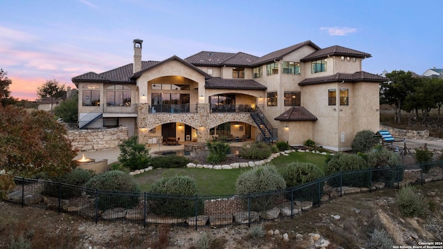 back house at dusk featuring a balcony and a patio area