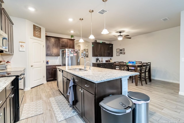 kitchen with a kitchen island with sink, sink, light wood-type flooring, appliances with stainless steel finishes, and dark brown cabinets