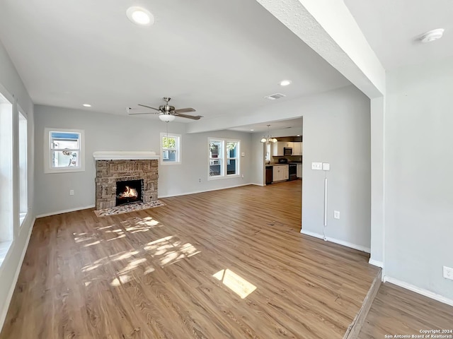 unfurnished living room featuring ceiling fan, a stone fireplace, and wood-type flooring