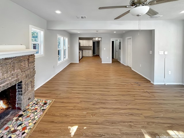 unfurnished living room featuring a fireplace, light hardwood / wood-style flooring, and ceiling fan with notable chandelier