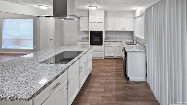 kitchen featuring light stone countertops, dark hardwood / wood-style flooring, island range hood, sink, and black appliances