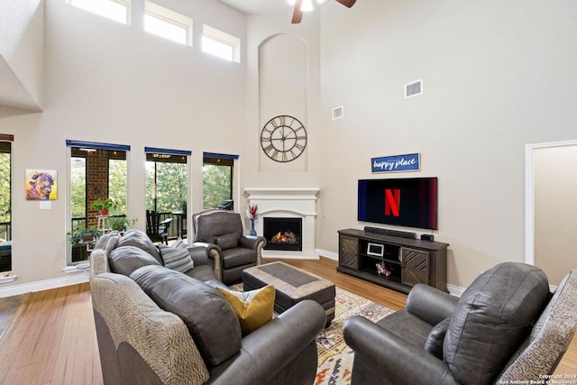 living room with ceiling fan, a towering ceiling, a healthy amount of sunlight, and light hardwood / wood-style floors