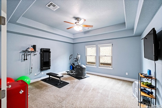 workout area featuring carpet, ceiling fan, a textured ceiling, and a tray ceiling