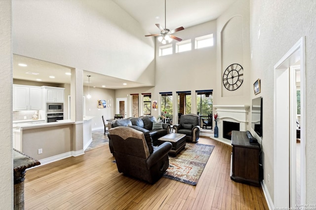 living room with ceiling fan, light hardwood / wood-style flooring, and a towering ceiling