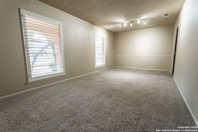 empty room with carpet floors, a textured ceiling, and rail lighting