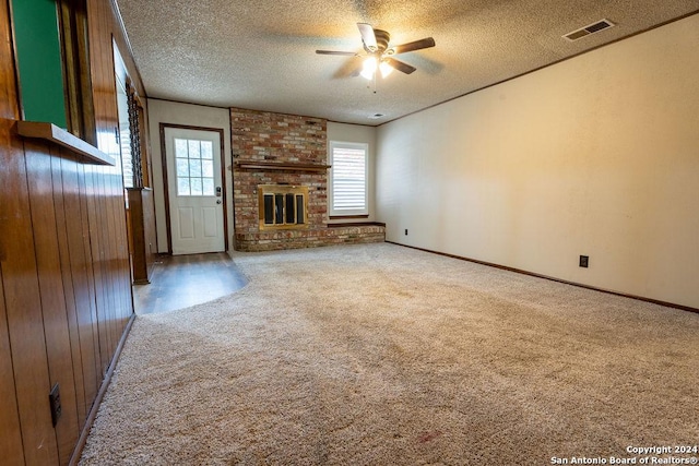 unfurnished living room featuring a fireplace, a textured ceiling, ceiling fan, and wood walls