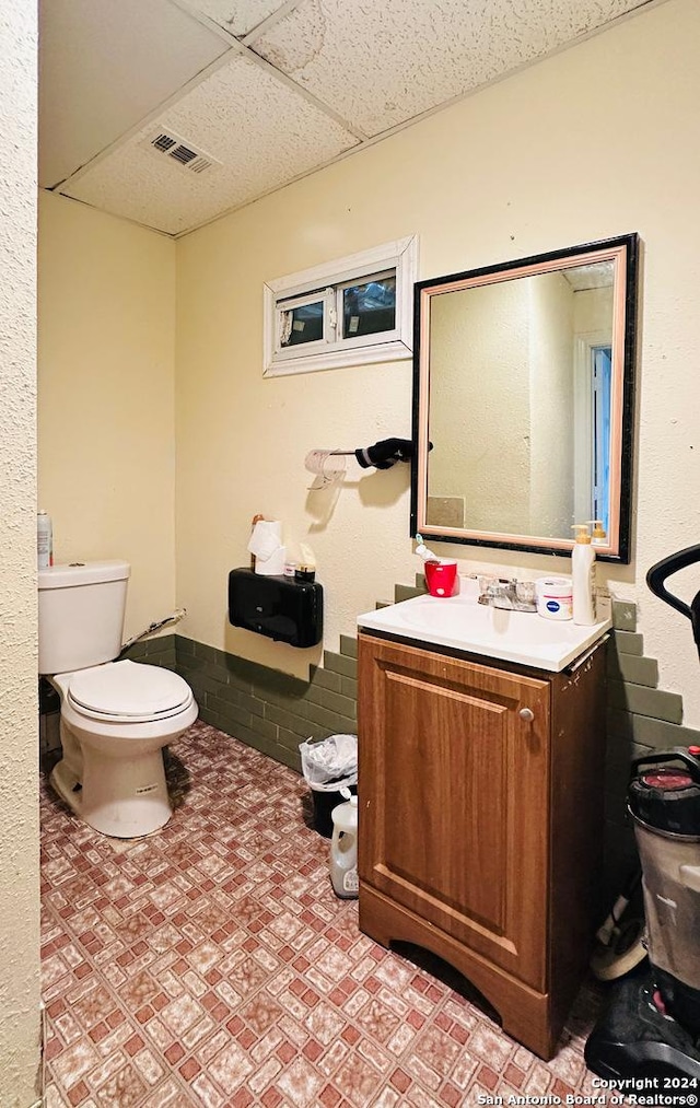 bathroom with a drop ceiling, toilet, and vanity