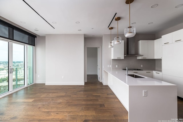 kitchen featuring decorative backsplash, dark hardwood / wood-style flooring, wall chimney range hood, pendant lighting, and white cabinets