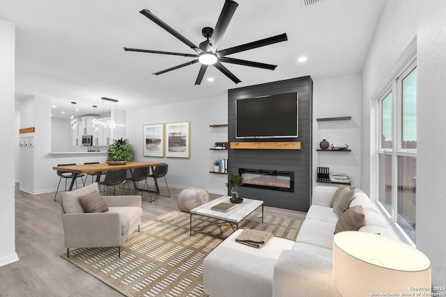 living room with a large fireplace, light hardwood / wood-style flooring, and ceiling fan